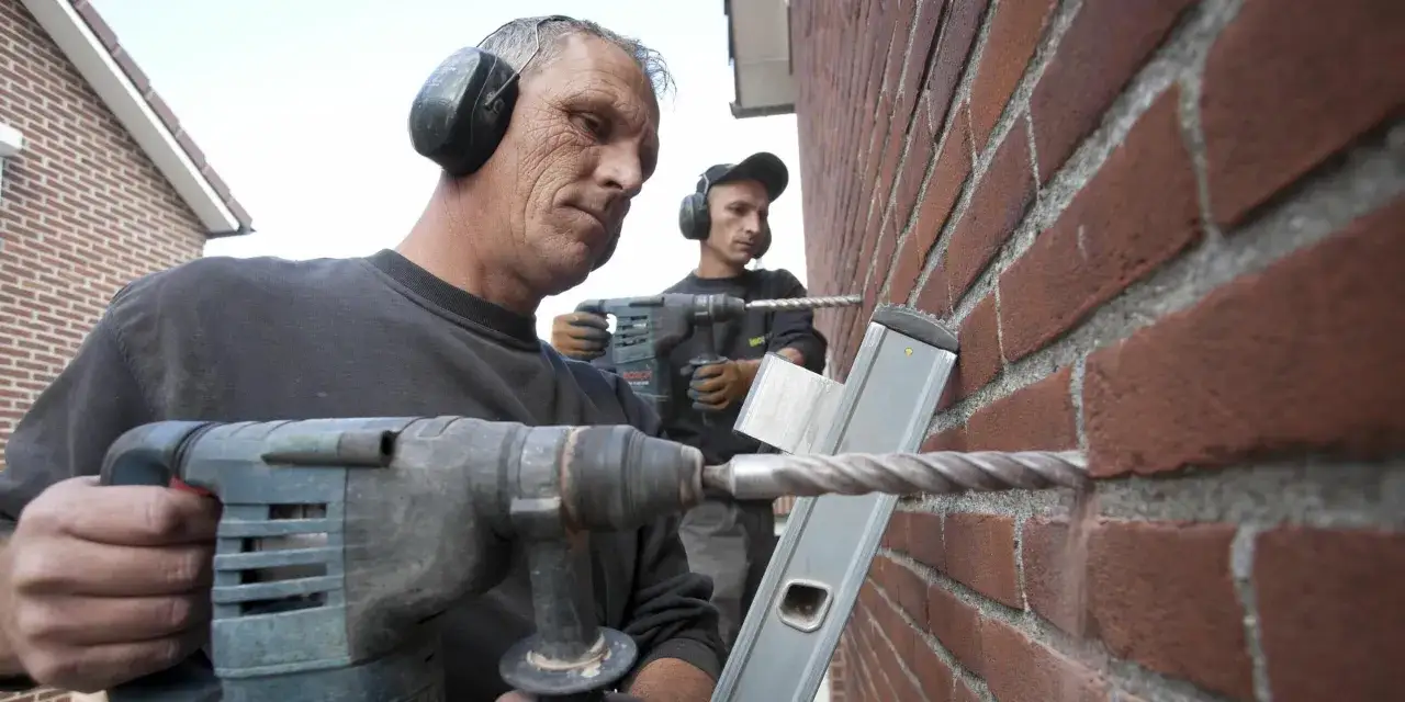 Deux ouvriers forent un mur de briques pour l'isolation par injection. Prix et devis pour une maison bien isol&eacute;e.