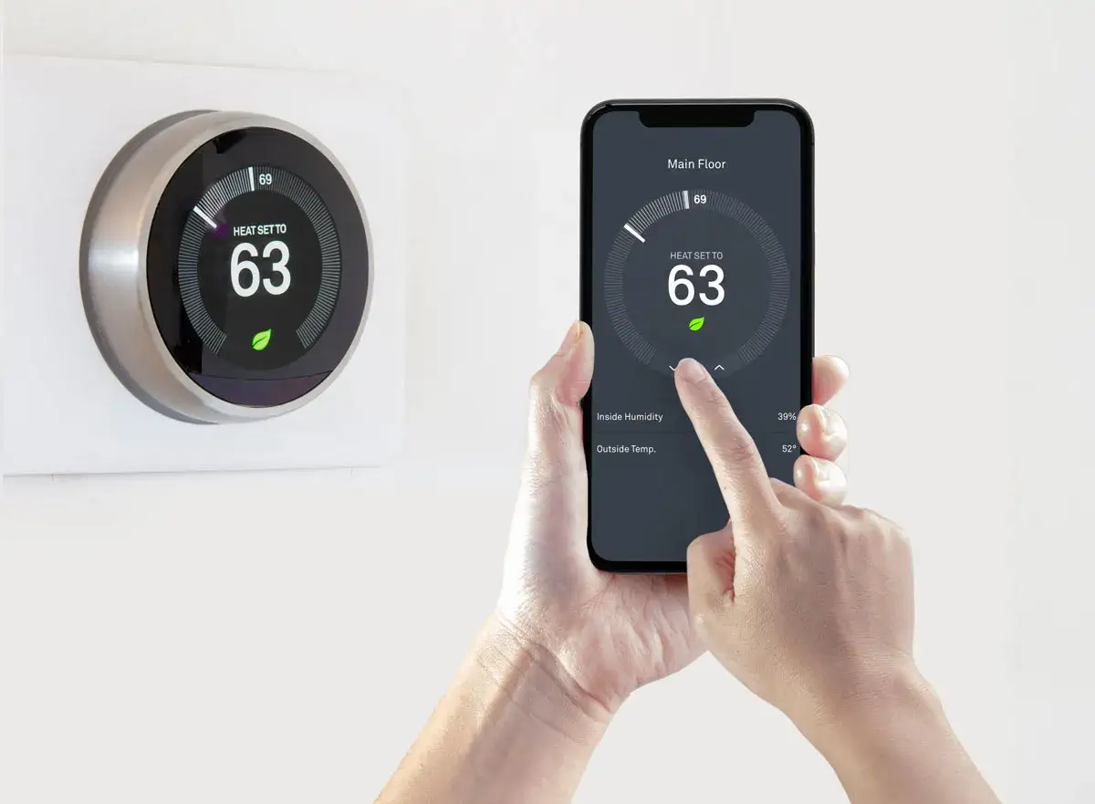 Une main utilise un smartphone pour piloter sa climatisation &agrave; distance. L'&eacute;cran affiche la temp&eacute;rature int&eacute;rieure et ext&eacute;rieure.