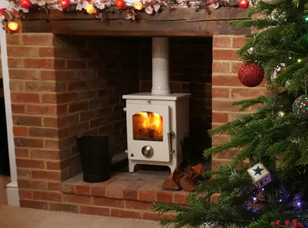 Installation d'un poêle à granulé blanc dans une cheminée en briques, avec un conduit existant. Un sapin de Noël décoré est à droite.