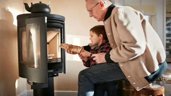 Un grand-père aide son petit-fils à charger du bois dans un poêle. Une alternative au chauffage au fioul, mais attention aux dangers du feu.