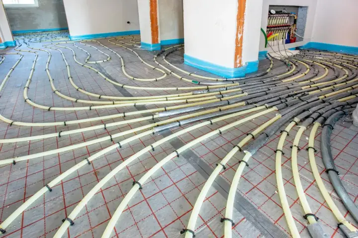 Installation de tubes pour un système de chauffage au sol. Les tuyaux jaunes sont fixés sur une grille rouge, prêts à être recouverts.